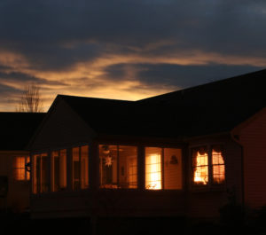 Looking into a house as the sun goes down. Lights inside duplicate sky lights behind. Warm glow of home.