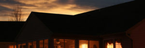 Looking into a house as the sun goes down. Lights inside duplicate sky lights behind. Warm glow of home.