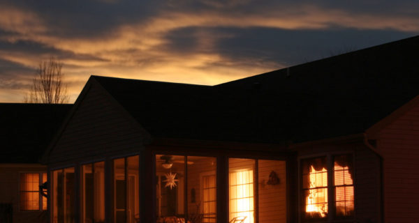 Looking into a house as the sun goes down. Lights inside duplicate sky lights behind. Warm glow of home.